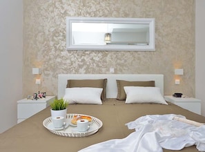 Ein Schlafzimmer mit einem Bett, Nachttischen, einer Ablage mit Tassen und Speisen sowie einem Spiegel an der Wand.
