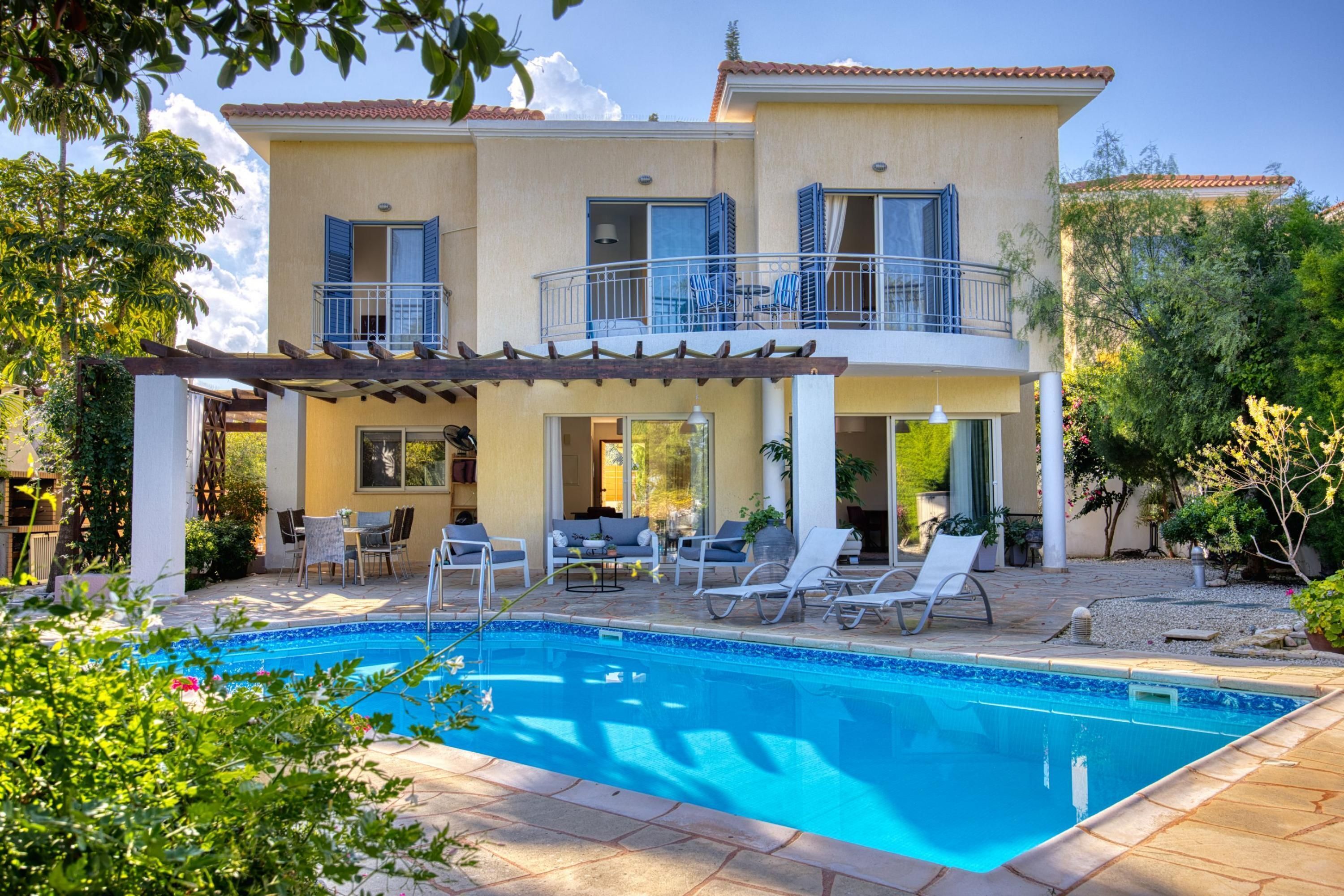 Una casa de dos pisos con piscina, mobiliario exterior y un patio cubierto.