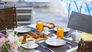 A breakfast table with croissants, orange juice, and coffee, set outdoors near a pool. - Latchi Aria Villa in Latchi (Latchi)