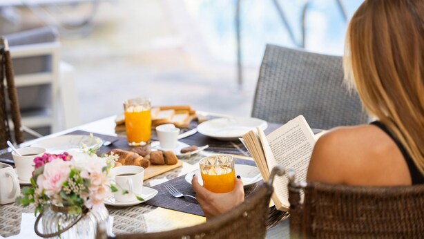 A breakfast setting with a table set for two, including a book, coffee, orange juice, and pastries. - Latchi Aria Villa in Latchi (Latchi)