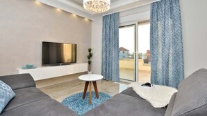 Ein modernes Wohnzimmer mit Flachbildfernseher, grauen Sofas, einem kleinen weißen Tisch und einer Chandelüster.