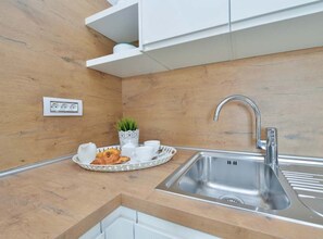 Eine moderne Küche mit Holzrückwand, Spüle aus Edelstahl und einer Schale mit Tassen und einem Gebäckstück.
