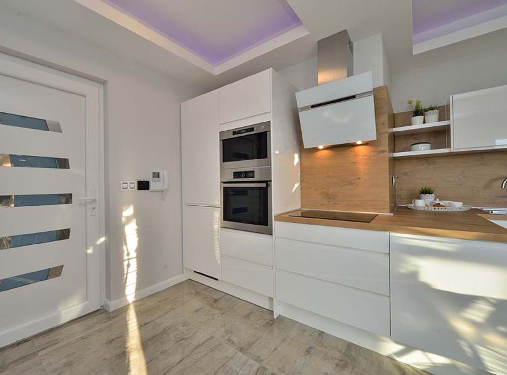 Cozinha moderna com eletrodomésticos embutidos, bancada de madeira e design de armários brancos.