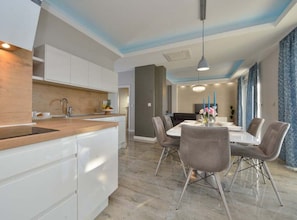 A modern kitchen with white cabinets, a wooden countertop, and a dining area with a table and chairs. - Villa Marija Exclusive Stay - Two Bedroom Apartment with Terrace 4 (Sukosan)