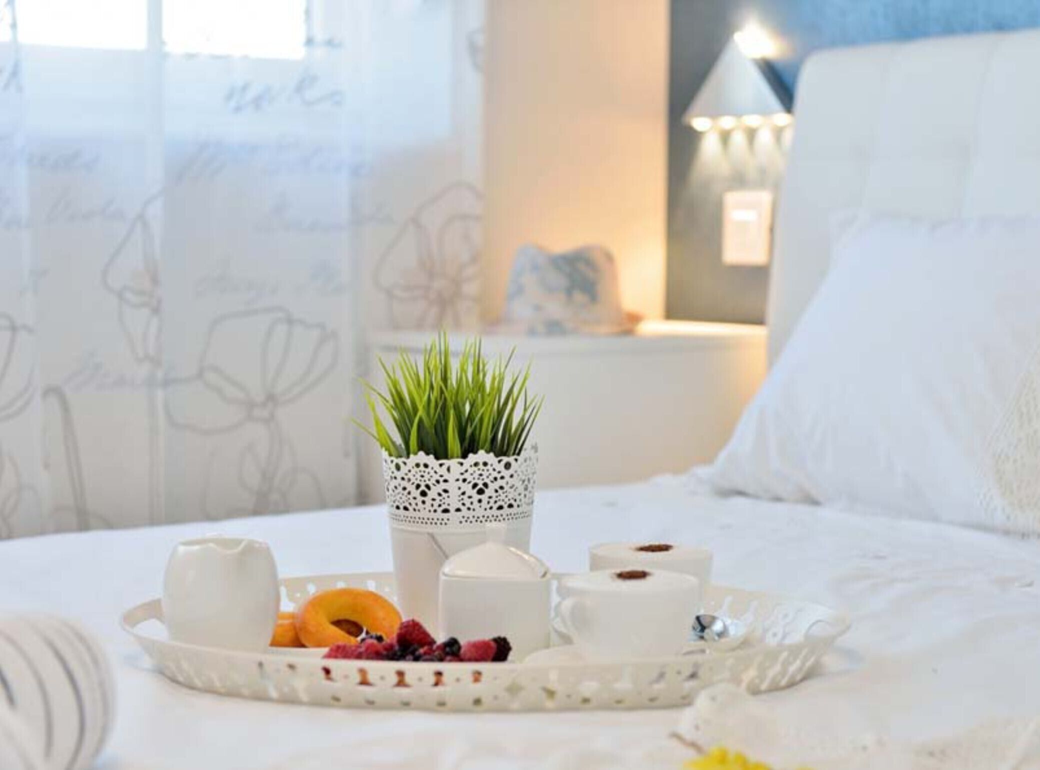 A neatly arranged breakfast tray with pastries, a cup, and a small potted plant on a bed.