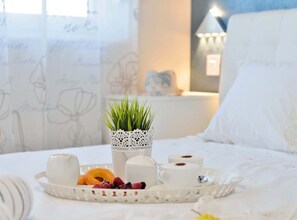 Ein ordentlich angerichtetes Frühstücksbrett mit Gebäck, einer Tasse und einem kleinen Topfpflanzchen auf einem Bett.