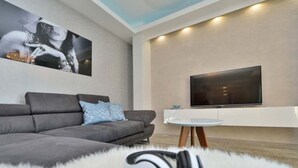 Ein modernes Wohnzimmer mit einem grauen Sofa, einem Flachbildfernseher und einem runden Couchtisch.