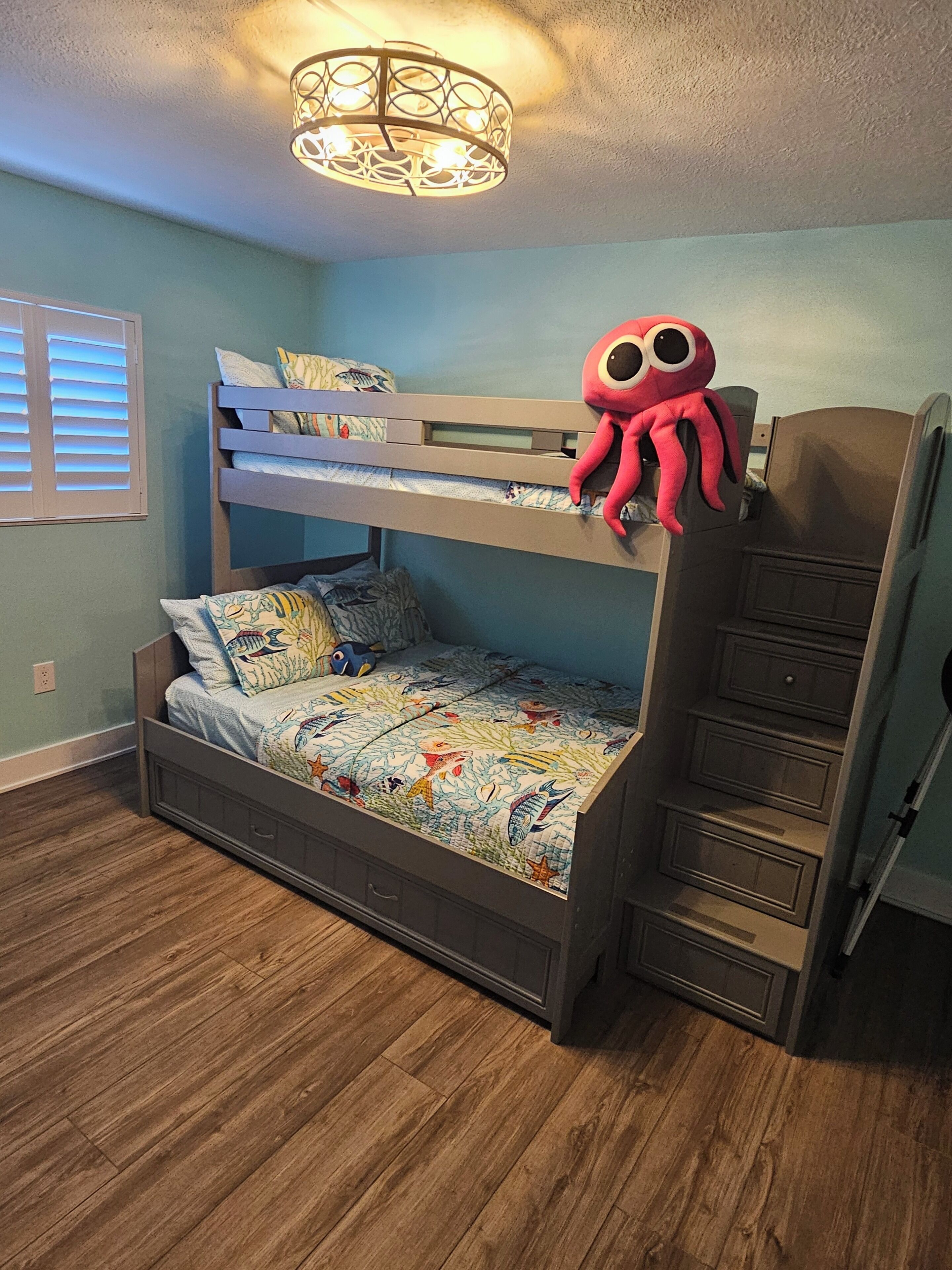 Un lit superposé avec une tête de lit décorative, un jouet en peluche représentant un poulpe et une couvre-lit à motifs.