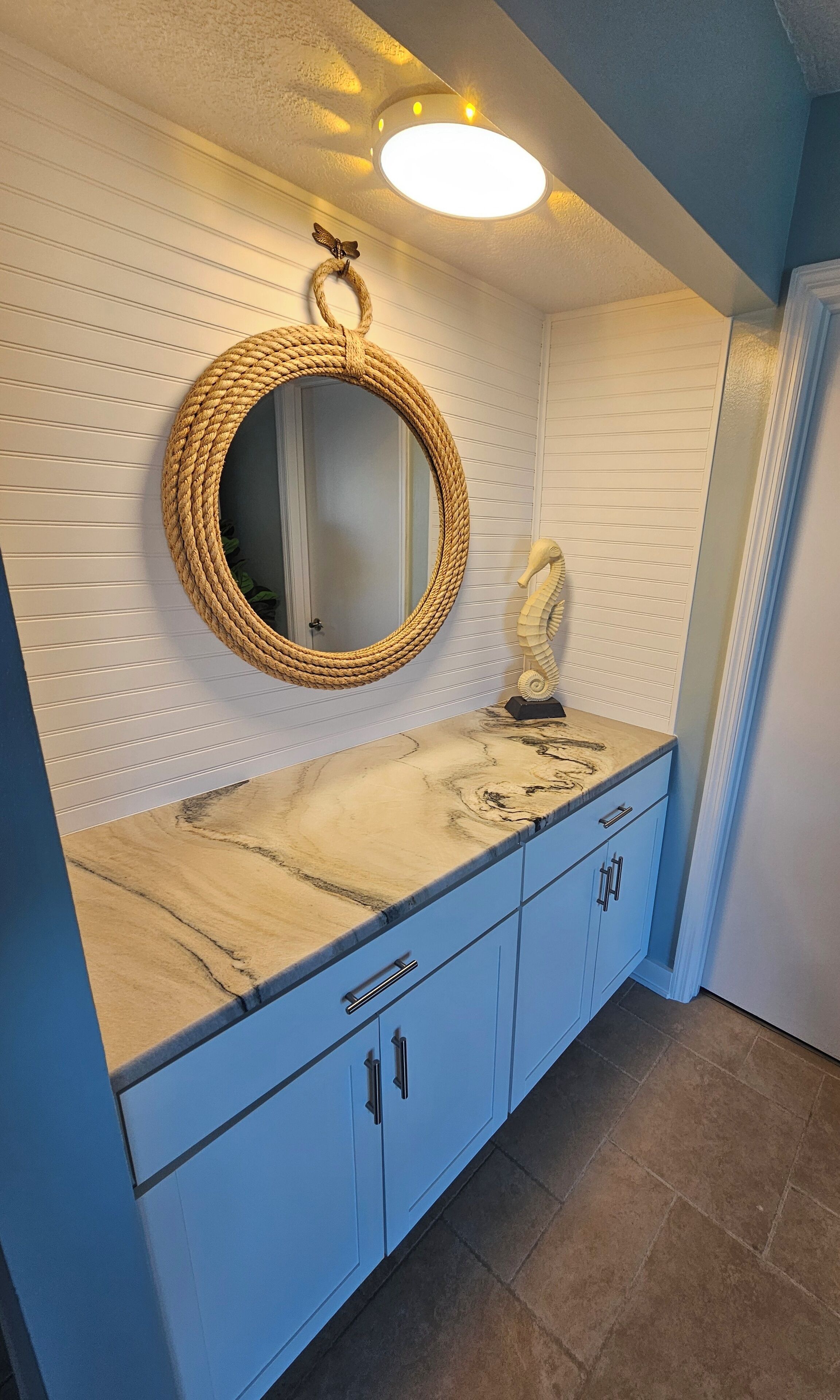 A bathroom with a round woven mirror, a seahorse sculpture, and a marble countertop.