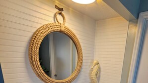 Um banheiro com um espelho redondo de fibra natural, uma escultura de cavalo-marinho e bancada de mármore.