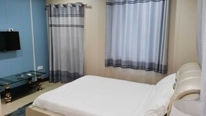 Una camera da letto con un letto, un tavolino in vetro, una TV a muro e due tende.