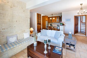 A living room with a sofa, a coffee table, and a bookshelf. There is a kitchen visible in the background. - Siorra Elena in Paxi (Paxi)