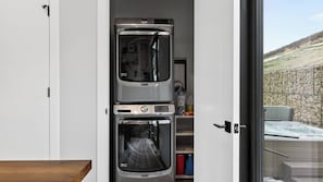 A compact kitchen with a built-in oven and microwave, a small shelf with kitchen essentials, and a view of a stone wall and outdoor area. - Apex Ridge Retreat by Avantstay Private Hot Tub + Fireplace + Mountain Views + Near Deer Valley East (Kamas)