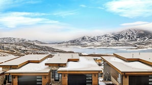 Un bâtiment moderne doté d’un toit plat, de grandes fenêtres et offrant une vue sur des montagnes enneigées et un lac.