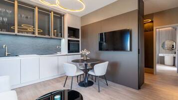 A modern kitchen with a built-in oven, a dining area with a round table and chairs, and a large flat-screen TV mounted on the wall.