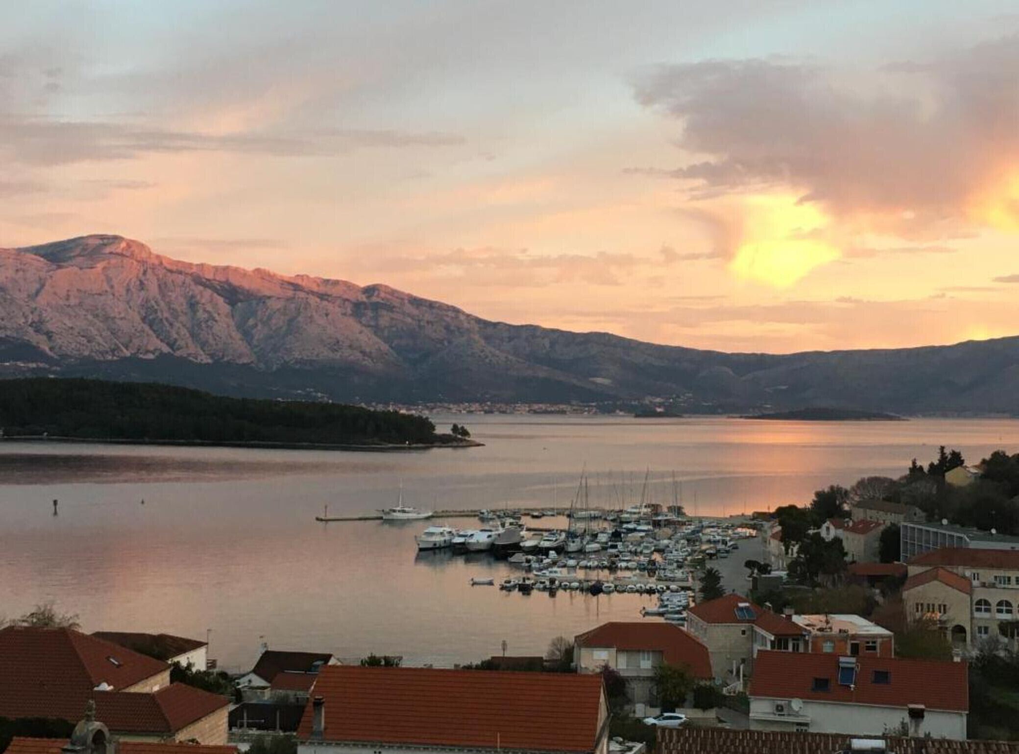 A marina with boats docked, surrounded by residential buildings and mountains in the background.