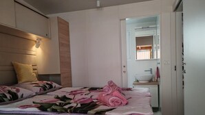 Quarto moderno com cama, abajur, banheiro pequeno com pia e espelho.