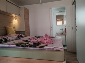 Un dormitorio moderno con cama, lámpara de noche, baño pequeño con lavamanos y espejo.
