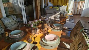 Uma mesa de jantar de madeira posta com pratos, copos e talheres, rodeada por cadeiras com almofadas.