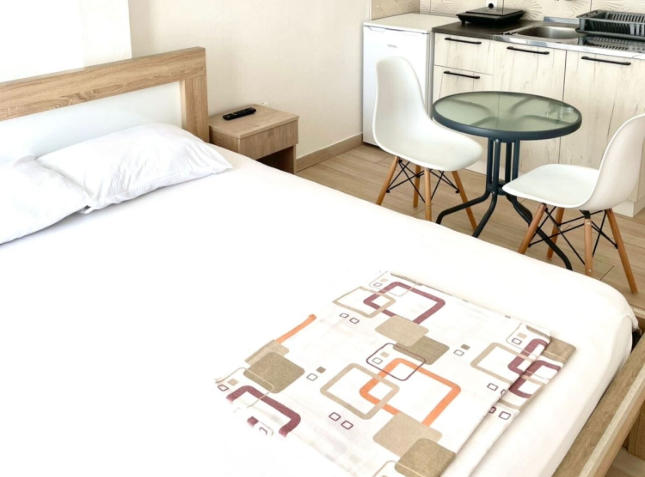 Ein Hotelzimmer mit Bett, einem kleinen Nachttisch, einem Schreibtisch mit Stuhl, einem Glastisch und einer Küchenzeile.
