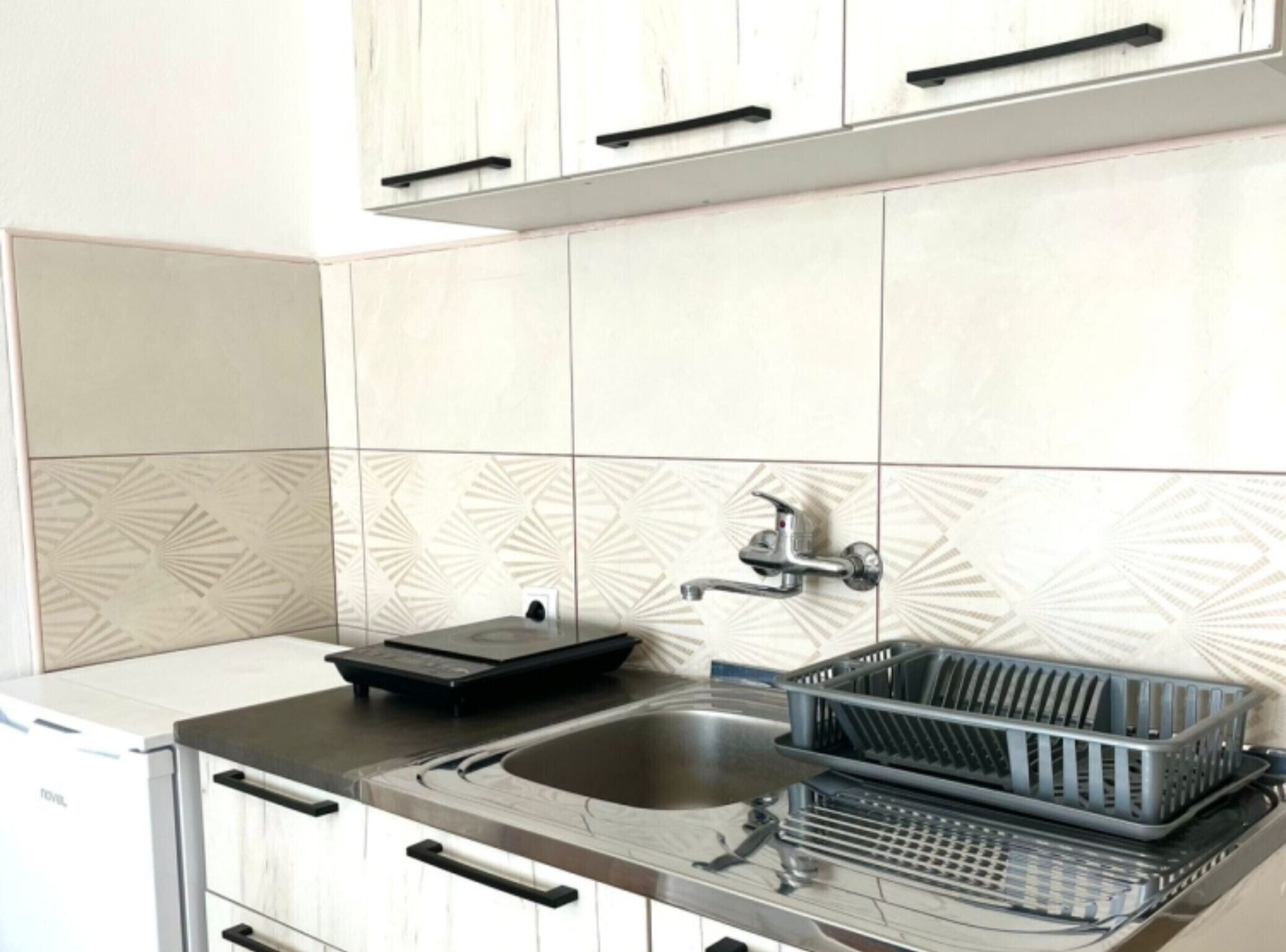 Une cuisine avec des carreaux blancs, un évier en acier inoxydable, un égouttoir et un appareil électroménager noir.