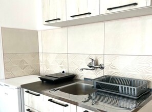 A kitchen with white tiles, a stainless steel sink, a dish rack, and a black appliance. - Comfort Apartments N - Studio apartment 4 (Sutomore)