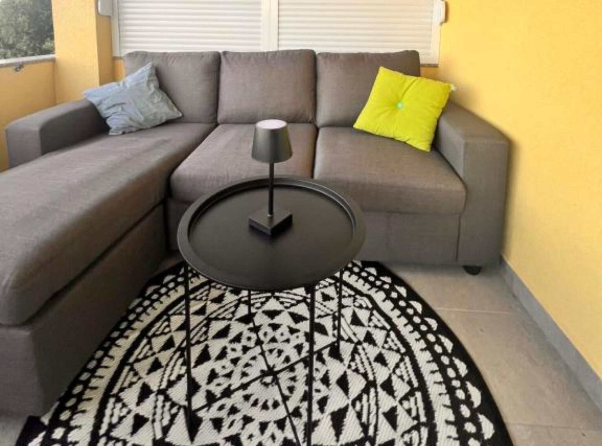 A corner living area with a gray sofa, a round coffee table, and a patterned rug.