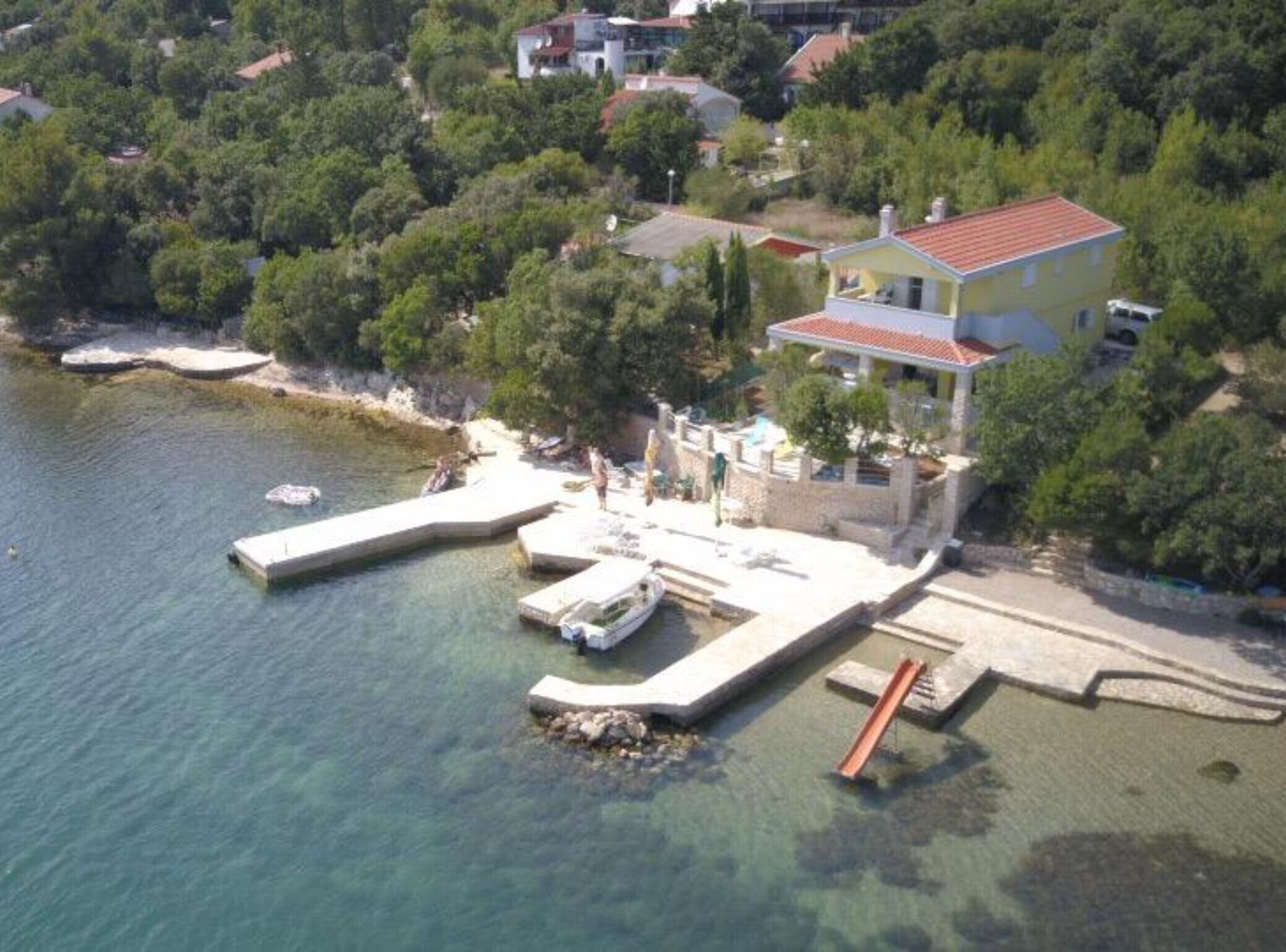 A coastal property with a dock, a small boat, and a house with a red roof.