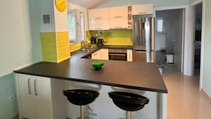 Eine moderne Küche mit einer zentralen Kochinsel, zwei Barhocker, einem Edelstahlkühlschrank und einer gelben Rückwand.