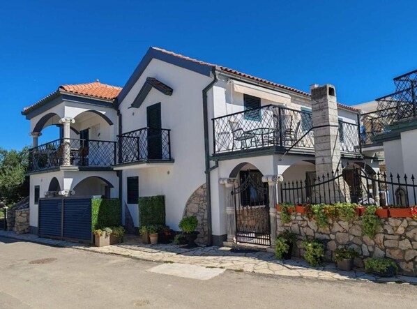 Una casa de dos pisos con balcón, pared de piedra y un portón.
