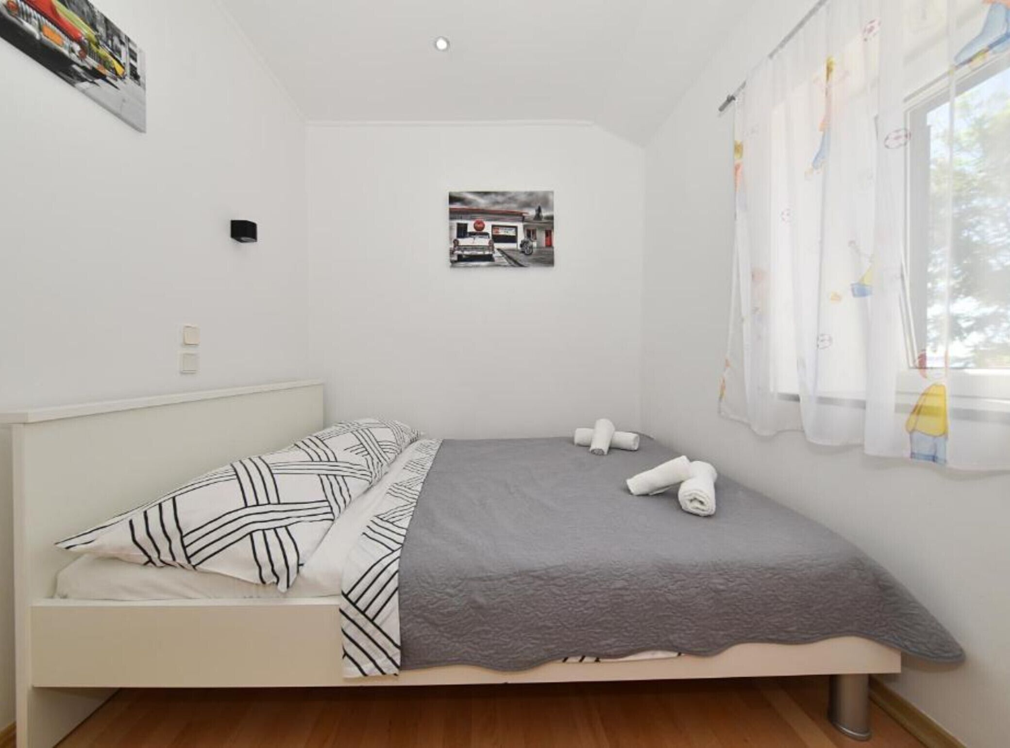 A small, neatly arranged bedroom with a bed, pillows, a blanket, and a framed picture on the wall.
