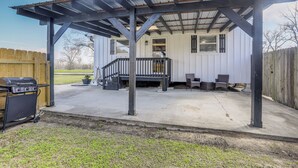 A covered patio with a grill, outdoor seating, and a wooden fence. - Riverfront Ventress Home w/ Patio & Shared Pier (Ventress)