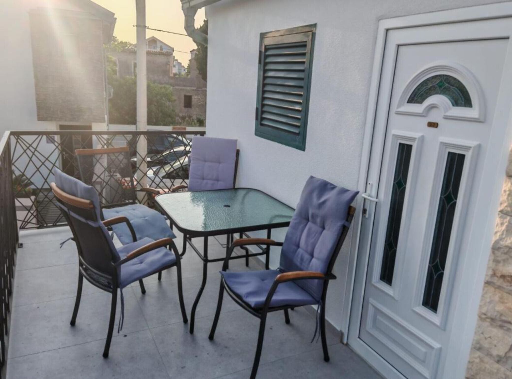 Un balcone con tavolo e quattro sedie, una porta bianca con finestra e un cancello in metallo.