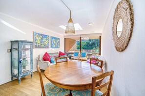 Un coin repas comprenant une table ronde en bois, des chaises, un meuble vitré et des œuvres d’art colorées accrochées aux murs.