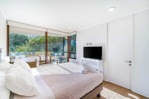 Une chambre moderne avec un grand lit, une télévision et un balcon donnant sur un paysage verdoyant.