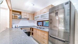 A modern kitchen with a stainless steel refrigerator, wooden cabinets, and a granite countertop.
