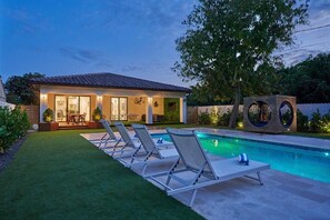 Una casa moderna con piscina, un patio con sillones de descanso y un césped bien cuidado.