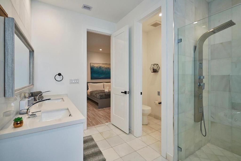 Un baño moderno con cabina de ducha de vidrio, un lavamanos blanco con espejo y un inodoro a la vista.