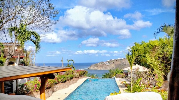 A pool with a view of the ocean, surrounded by greenery and a wooden deck. - Casa Altavista 3 Bedroom 4 Bath Oceanview Home with 2 Pools, Patios, and Balconies (San Juan del Sur)