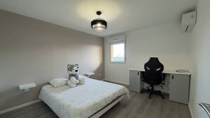 Ein Schlafzimmer mit einem Bett, einem Schreibtisch, einem Stuhl, einem Fenster und einer Deckenleuchte.