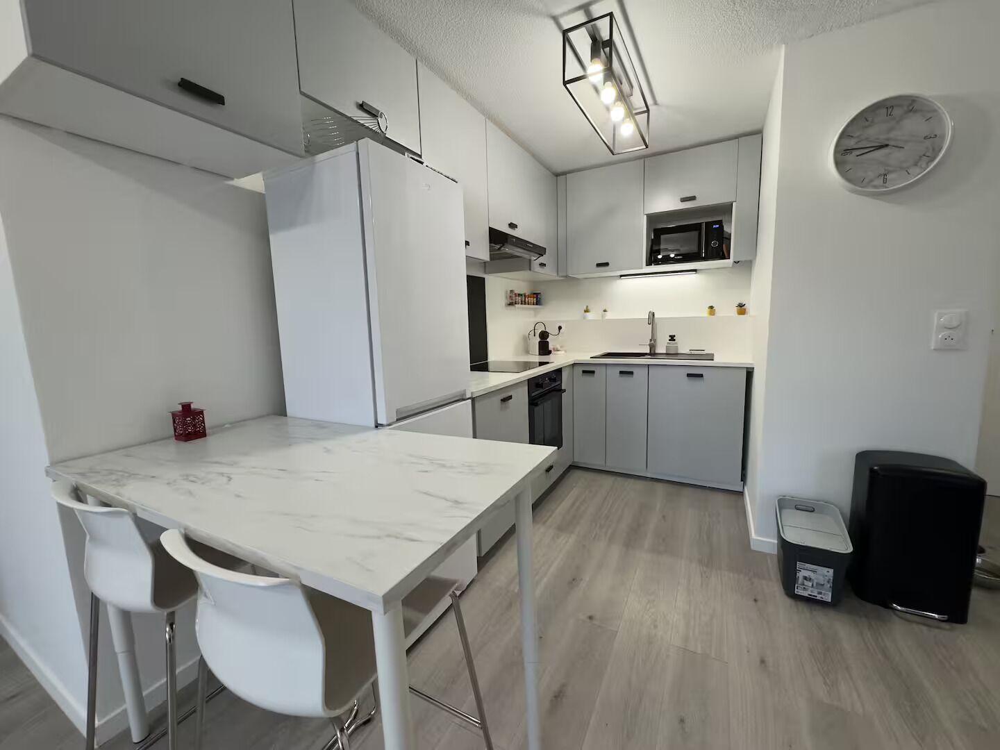 Uma cozinha moderna com armários brancos, bancada de mármore e um cesto de lixo preto.