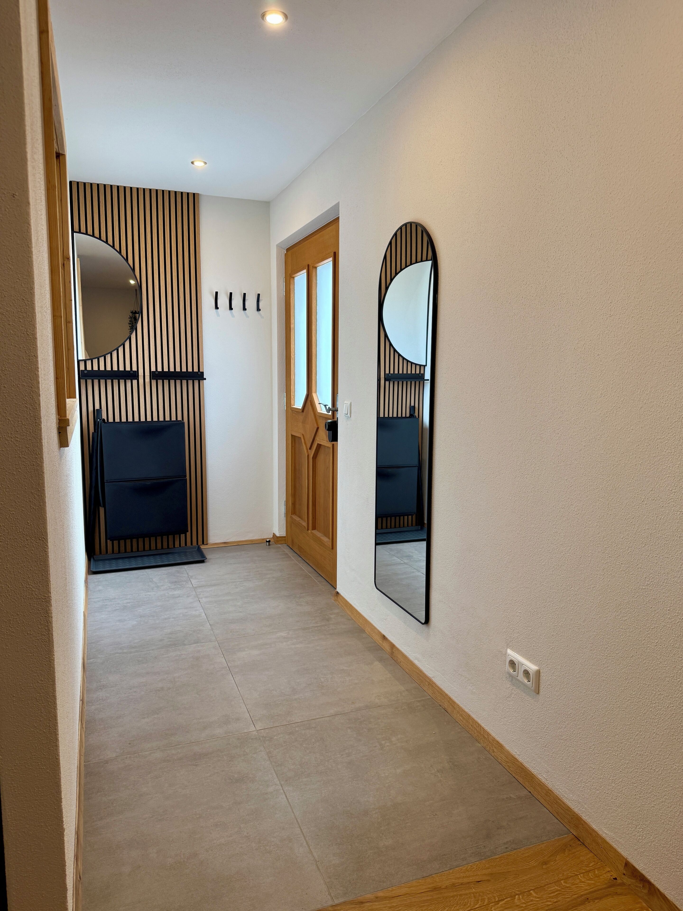 A hallway with a wooden door, a bench, and two wall-mounted mirrors.