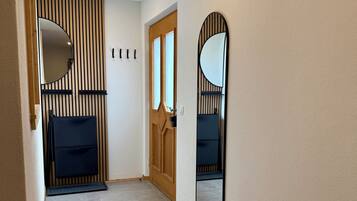 A hallway with a wooden door, a bench, and two wall-mounted mirrors.