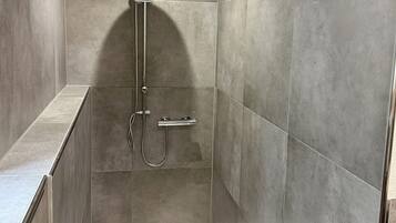 A walk-in shower with a handheld showerhead, a handheld showerhead, and a wall-mounted faucet.