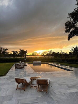 An outdoor pool area with a sunset view, surrounded by greenery and equipped with wooden lounge chairs. - Enjoy Magnificent Views in this Private, Quiet, and Serene Waterfront Retreat (Vero Beach)