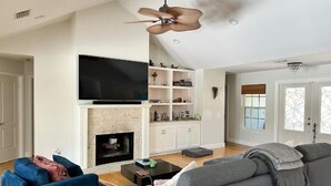 Una sala de estar con chimenea, televisor y ventilador de techo.