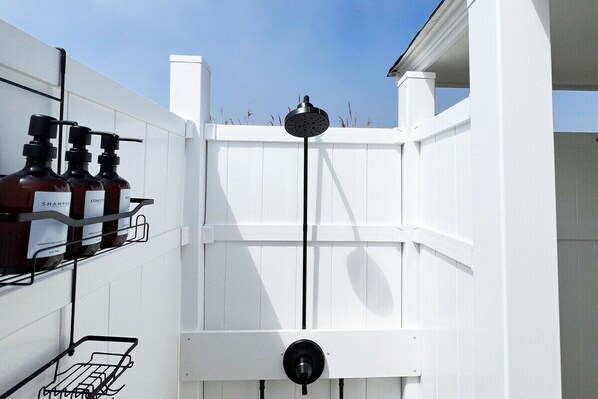 A white fence with a black hose and a metal rack holding bottles.