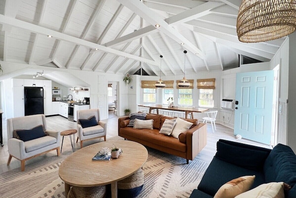 A spacious living area with a high ceiling, a dining table, and a kitchen in the background.