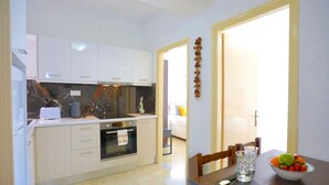 Uma cozinha moderna com armários brancos, painel de fundo em mármore e uma área de jantar com mesa posta para dois.
