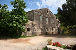 A rustic stone building with multiple windows and a gravel driveway. - Evanna House in Saint Stephanos (Agios Stefanos)